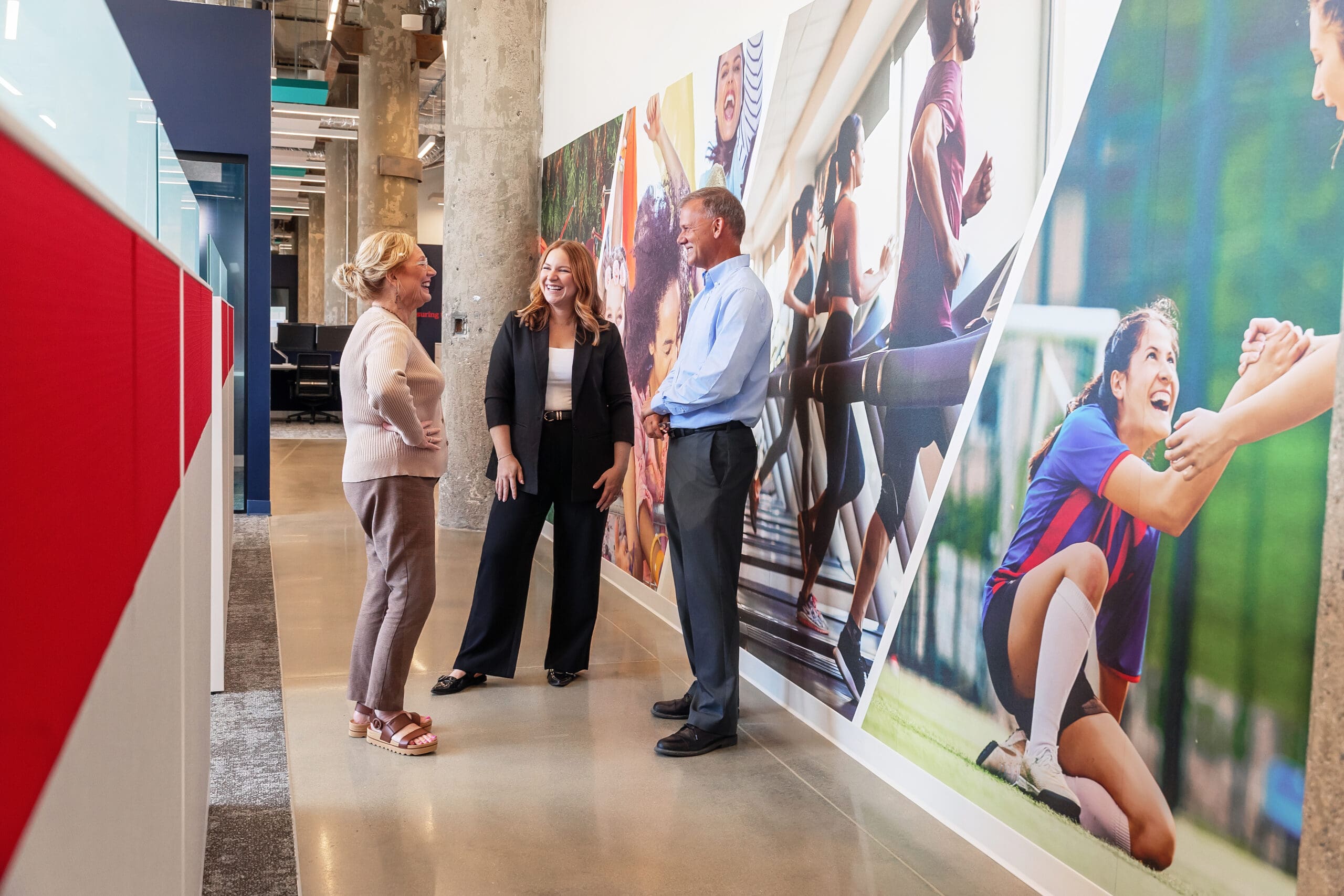 group of people standing and laughing in a corporate office hallway.