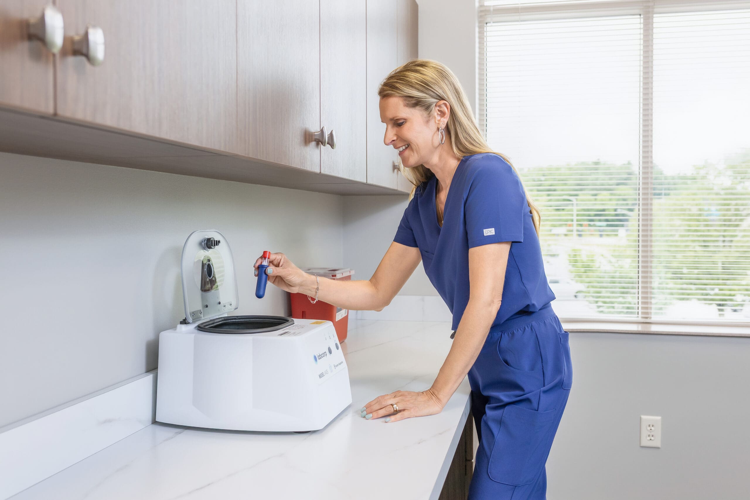 woman in scrubs leaning on counter testing blood sample.